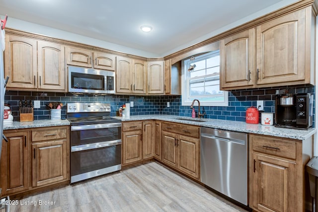 kitchen featuring sink, stainless steel appliances, light hardwood / wood-style floors, and light stone countertops