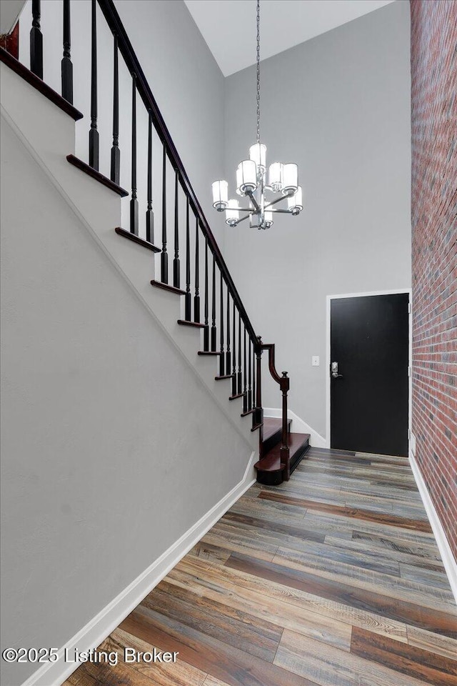 foyer entrance featuring hardwood / wood-style flooring, a towering ceiling, brick wall, and a notable chandelier