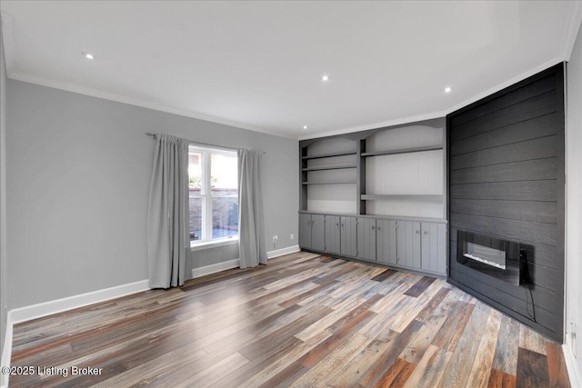 unfurnished living room with hardwood / wood-style floors, crown molding, and built in shelves