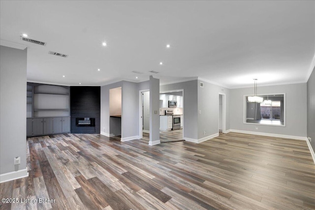 unfurnished living room featuring a notable chandelier, crown molding, a fireplace, and wood-type flooring