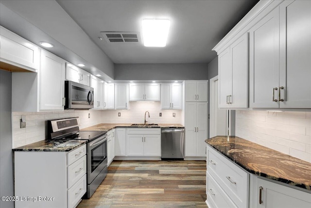 kitchen with white cabinetry, sink, dark stone counters, stainless steel appliances, and light hardwood / wood-style flooring