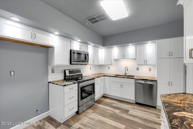 kitchen featuring white cabinetry, stainless steel appliances, sink, and dark stone countertops