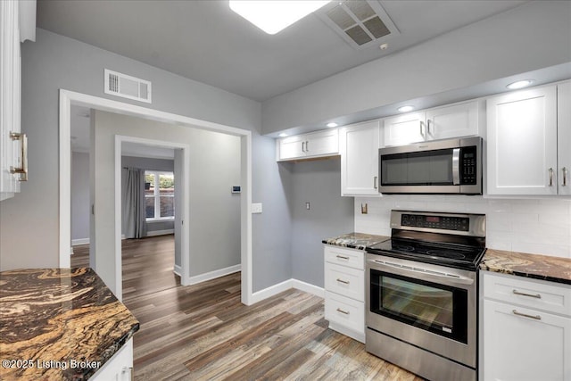 kitchen featuring stainless steel appliances, wood-type flooring, white cabinets, decorative backsplash, and dark stone counters