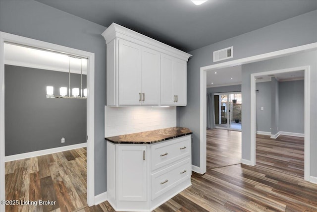 kitchen featuring backsplash, white cabinets, a chandelier, crown molding, and dark wood-type flooring