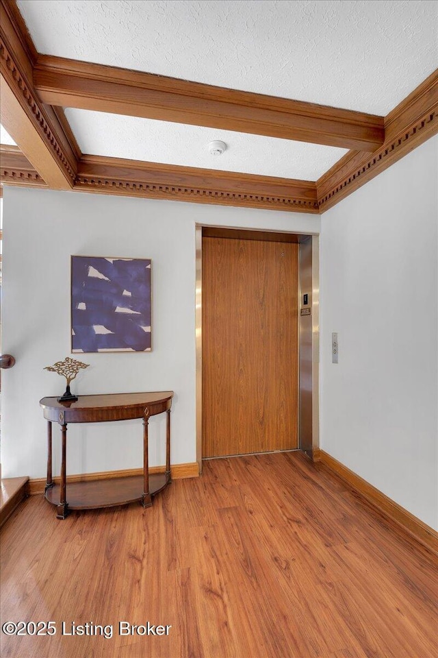 empty room with hardwood / wood-style flooring, elevator, beam ceiling, and a textured ceiling