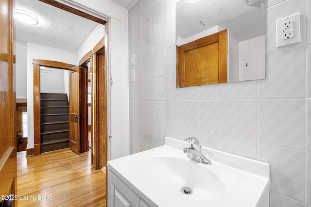 bathroom featuring vanity, hardwood / wood-style floors, a textured ceiling, and tile walls