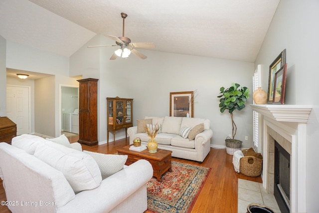 living room featuring independent washer and dryer, a tiled fireplace, vaulted ceiling, and light wood-type flooring