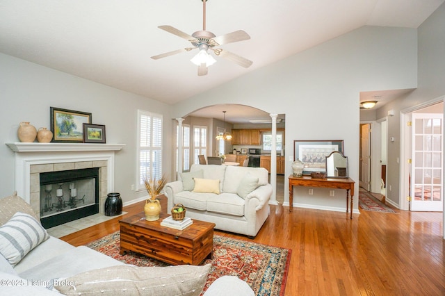 living room featuring lofted ceiling, a tiled fireplace, light hardwood / wood-style flooring, and ornate columns