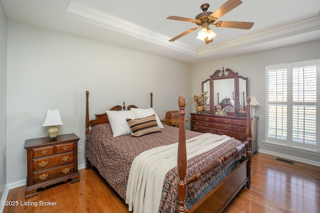 bedroom featuring ceiling fan, ornamental molding, a tray ceiling, and light wood-type flooring