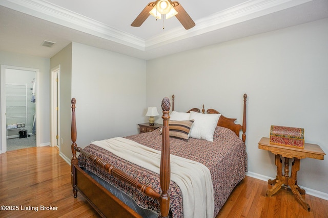 bedroom featuring crown molding, a raised ceiling, ceiling fan, and light wood-type flooring