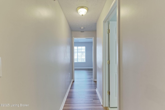 corridor featuring baseboards, a textured ceiling, and wood finished floors