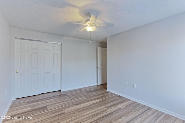 unfurnished bedroom featuring a textured ceiling, a closet, light wood-style flooring, and baseboards