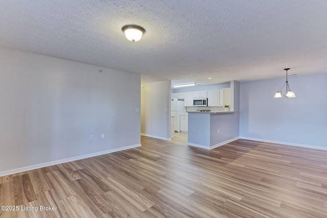 unfurnished living room with a textured ceiling, light wood finished floors, and baseboards