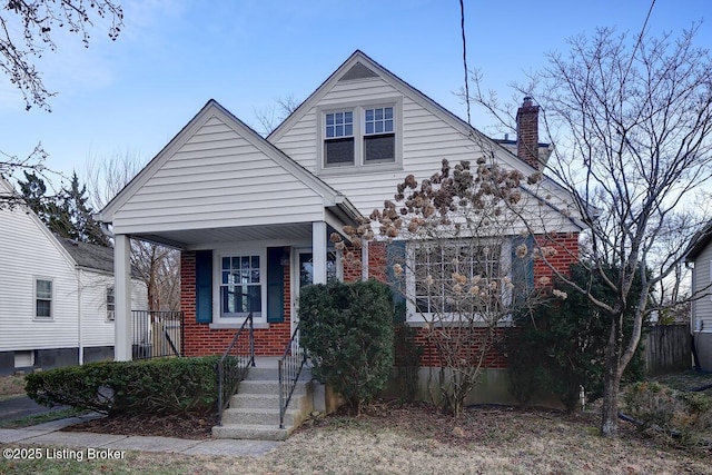 view of front facade featuring brick siding, covered porch, and a chimney