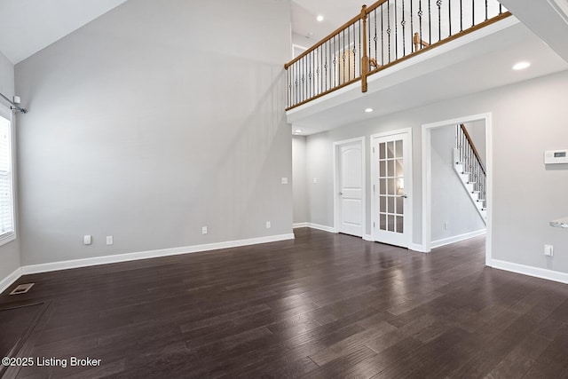 unfurnished living room featuring a towering ceiling and dark hardwood / wood-style floors