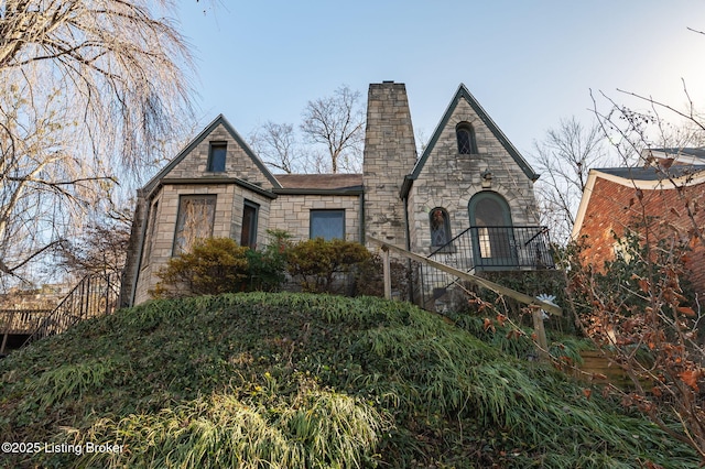 view of front of home featuring stone siding, stairway, and a chimney