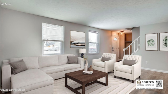 living room featuring light wood finished floors, stairway, baseboards, and a textured ceiling