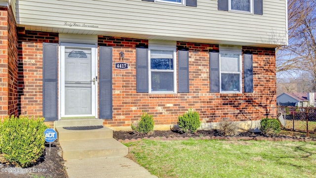 doorway to property featuring brick siding and fence