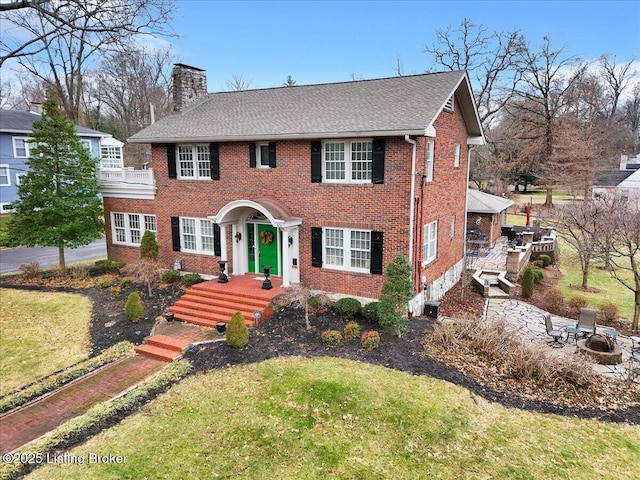 colonial home featuring a front lawn and an outdoor fire pit