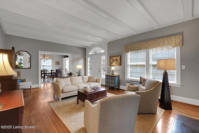 living room featuring a notable chandelier, beam ceiling, and light hardwood / wood-style floors