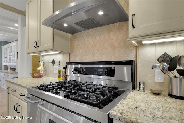 kitchen featuring wall chimney range hood, light stone countertops, decorative backsplash, and stainless steel gas stove