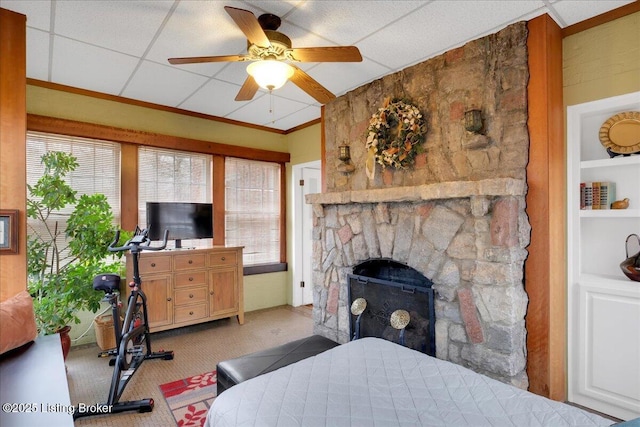 bedroom featuring a stone fireplace, light colored carpet, a drop ceiling, and ceiling fan