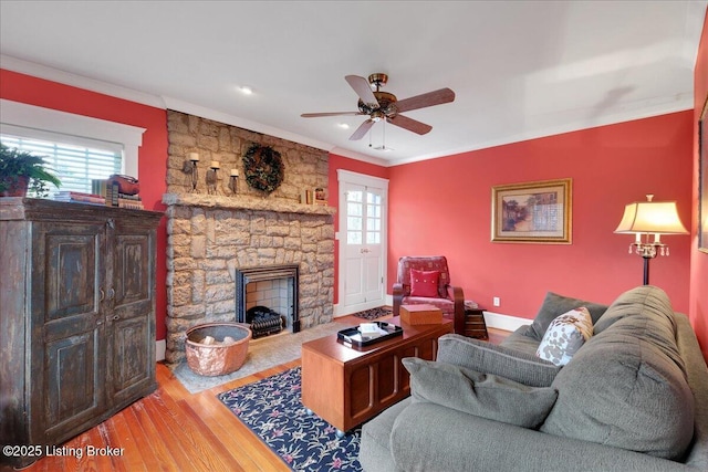 living room featuring ornamental molding, a stone fireplace, hardwood / wood-style floors, and ceiling fan