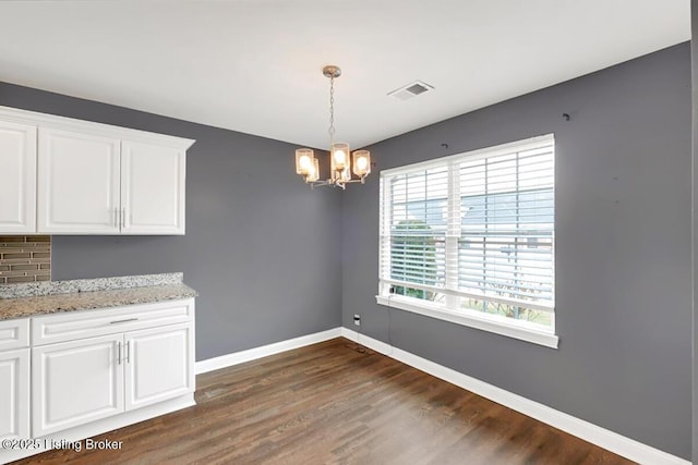 unfurnished dining area featuring dark wood-style flooring, visible vents, a notable chandelier, and baseboards