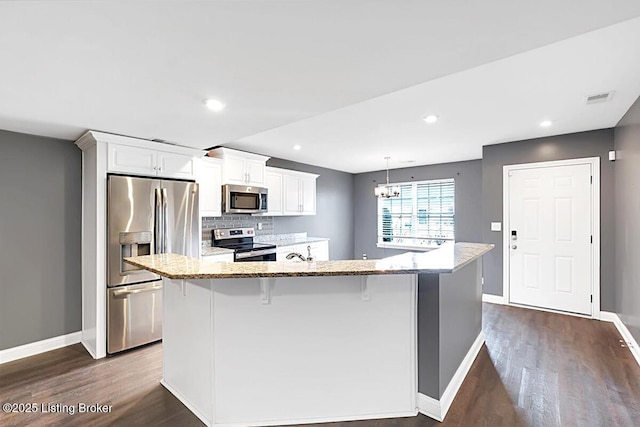 kitchen featuring light stone counters, stainless steel appliances, a spacious island, visible vents, and white cabinets