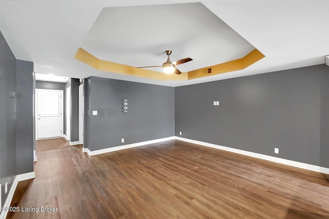 empty room with ceiling fan, visible vents, baseboards, dark wood-style floors, and a raised ceiling