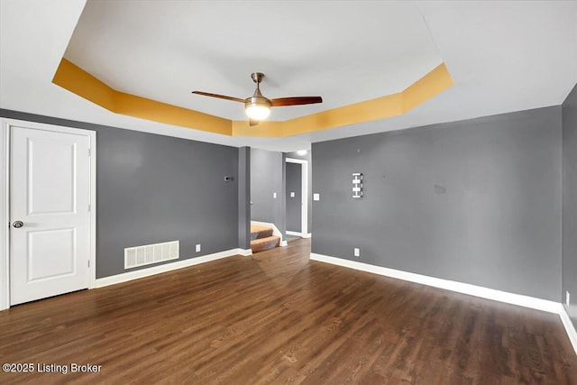 spare room featuring visible vents, baseboards, wood finished floors, stairs, and a tray ceiling