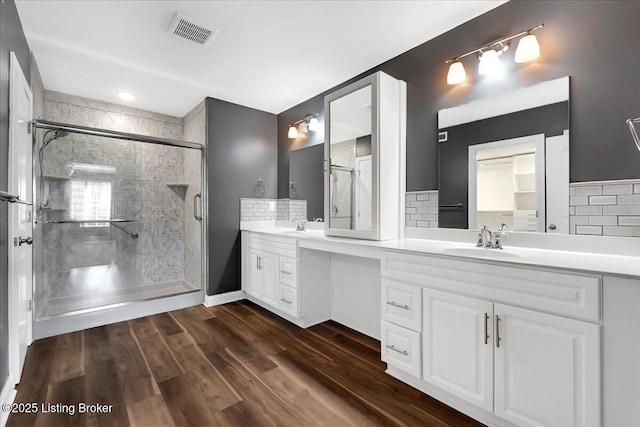 bathroom with double vanity, visible vents, a sink, a shower stall, and wood finished floors