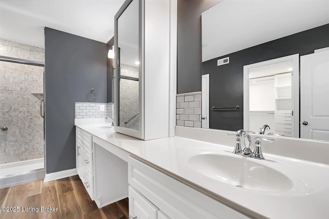 full bathroom with double vanity, decorative backsplash, a sink, a shower stall, and wood finished floors