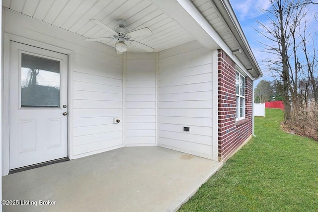 view of exterior entry featuring a ceiling fan, brick siding, and a yard