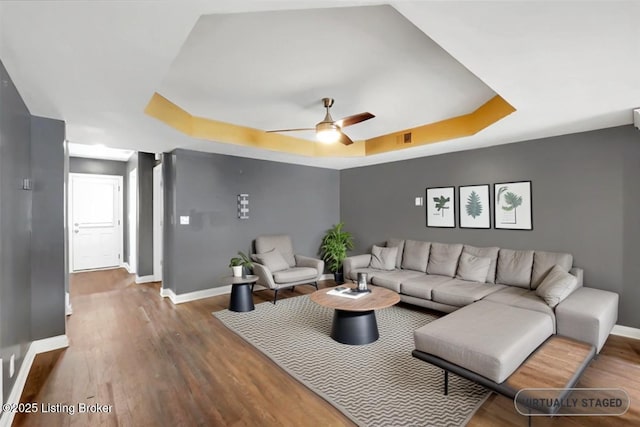 living area with baseboards, a tray ceiling, ceiling fan, and wood finished floors