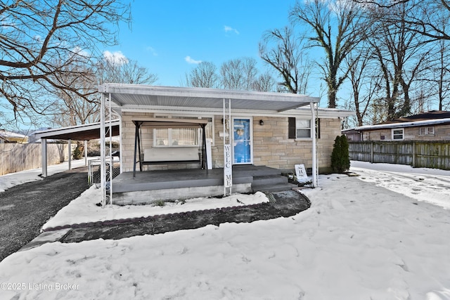 view of front of house with stone siding, fence, a porch, and a carport