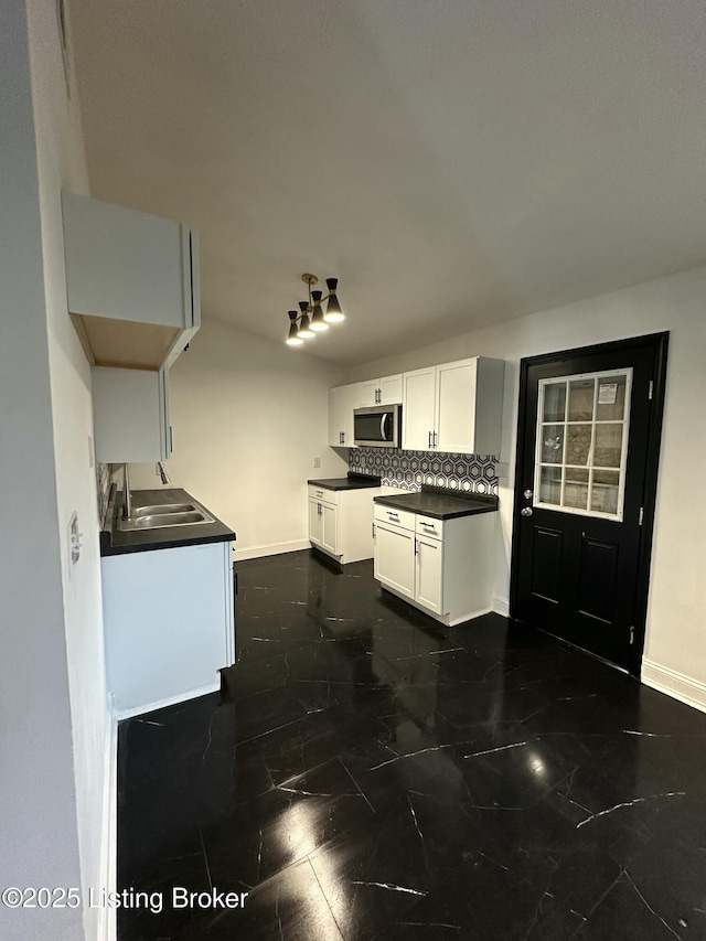 kitchen featuring a sink, white cabinetry, decorative backsplash, stainless steel microwave, and dark countertops