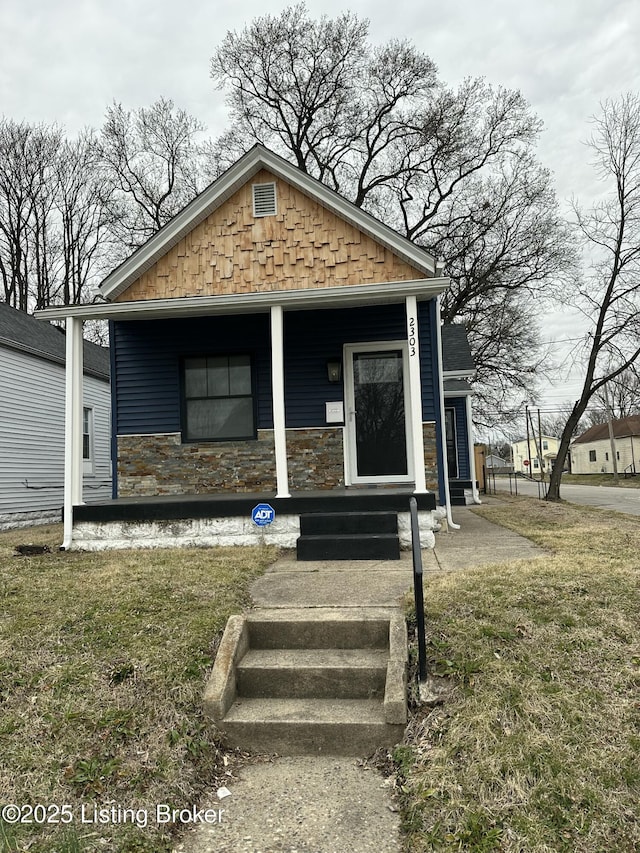 view of front of home with a front yard, stone siding, and covered porch