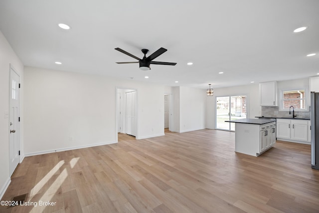 kitchen with sink, stainless steel refrigerator, white cabinetry, backsplash, and light wood-type flooring