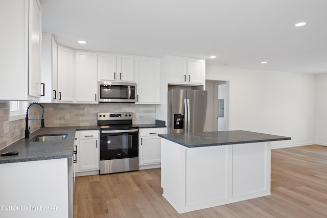 kitchen with sink, appliances with stainless steel finishes, white cabinetry, a center island, and light hardwood / wood-style floors