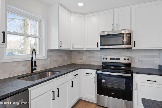 kitchen with tasteful backsplash, white cabinetry, sink, stainless steel appliances, and light wood-type flooring