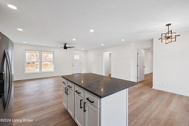 kitchen featuring decorative light fixtures, stainless steel fridge with ice dispenser, light wood-type flooring, dark stone counters, and white cabinets