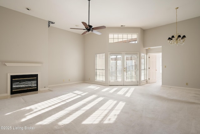 unfurnished living room featuring french doors, light colored carpet, ceiling fan with notable chandelier, and a high ceiling