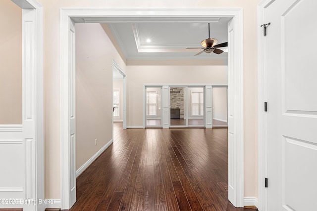 interior space with ceiling fan, ornamental molding, dark wood-type flooring, and a raised ceiling