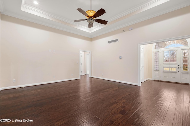 empty room with a tray ceiling, ornamental molding, dark wood-type flooring, and ceiling fan