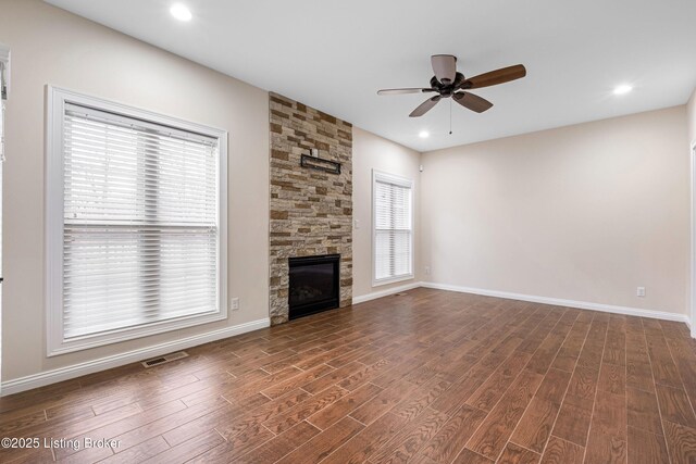 unfurnished living room with ceiling fan, a stone fireplace, and dark hardwood / wood-style floors