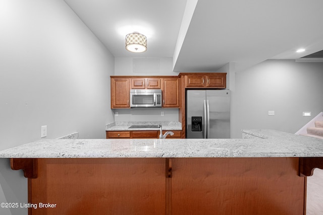 kitchen featuring stainless steel appliances, light stone counters, sink, a kitchen bar, and kitchen peninsula