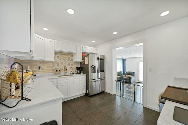 kitchen featuring stainless steel fridge, a sink, decorative backsplash, and white cabinetry