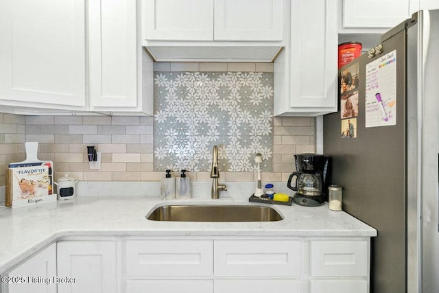 kitchen with a sink, white cabinets, backsplash, freestanding refrigerator, and light stone countertops