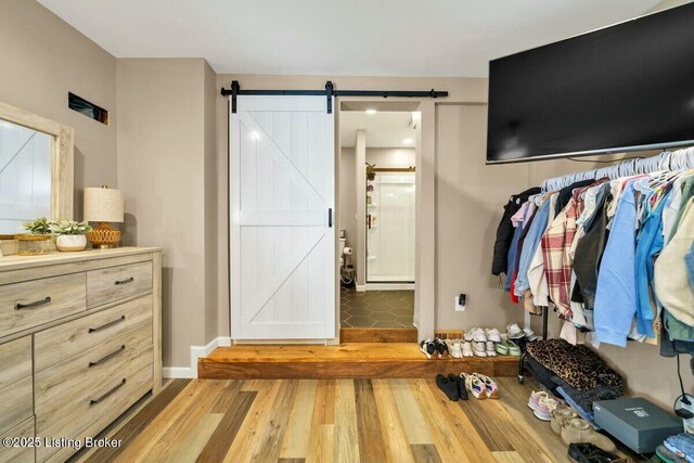 bedroom with a barn door, connected bathroom, baseboards, and wood finished floors